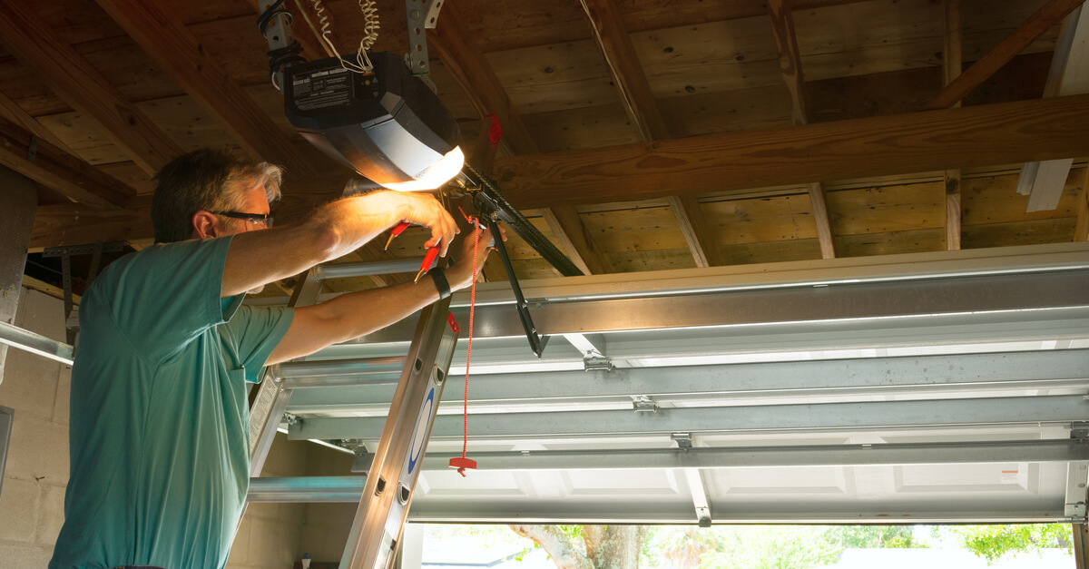 Professional automatic garage door opener repair service technician man working on a ladder at a home residential location making adjustments and fixing it while installing it.
